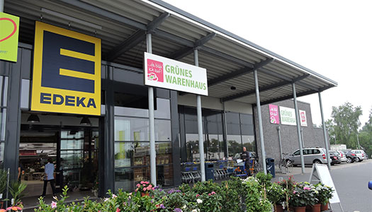 Eine Außenansicht eines Supermarktes mit dem Logo "EDEKA", auf dem Parkplatz stehen Autos und ein Fahrradständer.